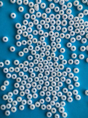 Mavi arkaplandaki beyaz boncuklara yakın çekim. Mücevher ve boncuk yapımında kullanılan malzemeler. Hedef vurma, mavi arkaplandaki nesneler.