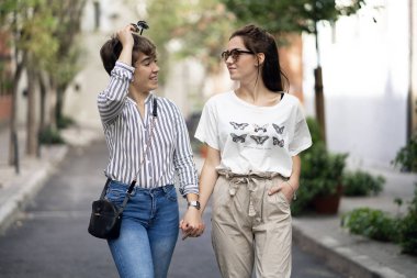 Genç bayan çift sokakta yürüyor ve gülüyor. Aralarına bakıyorlar.