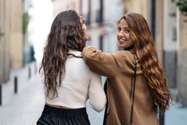 Sokakta birlikte yürüyen iki beyaz kadının stok fotoğrafı var. Biri geri geri gidiyor, diğeri de kameraya bakıyor. Onlar şık günlük kıyafetler giyiyorlar..