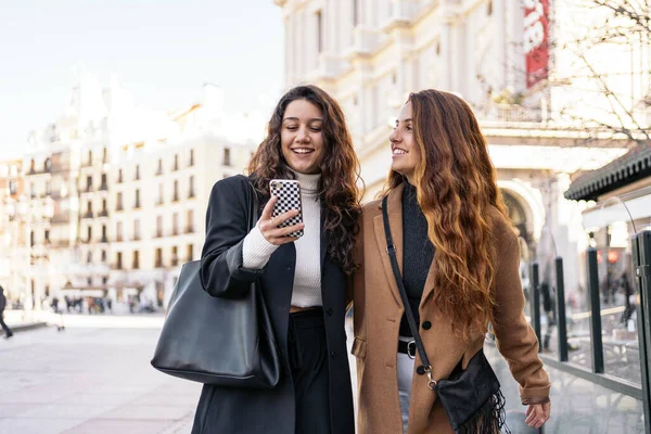 街中でスマホを使って歩いている2人の若い白人女性のストックフォト 笑ってる 彼らはスマートカジュアル服を着ている — ストック写真