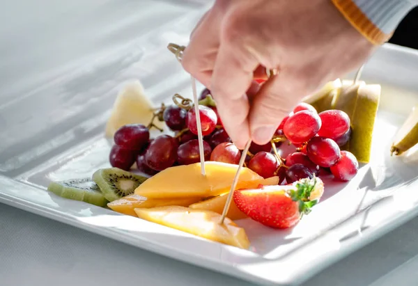 fruit plate with slices of melon, kiwi, strawberry, pear and grape berries and hand  taking treat