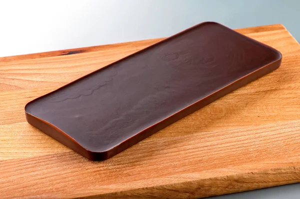 smooth chocolate bar on wooden board close-up against light background