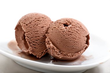 two frozen balls of chocolate ice cream on porcelain saucer close-up against white background  clipart