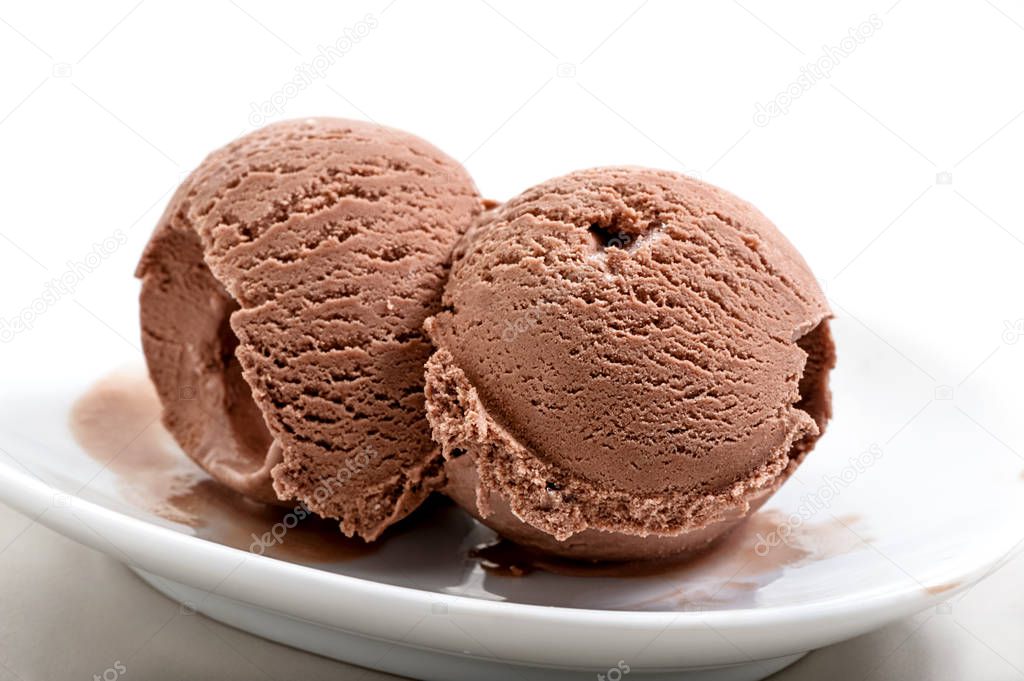 two frozen balls of chocolate ice cream on porcelain saucer close-up against white background 