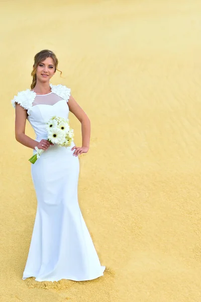 Gorgeous beautiful bride with flowers among the sand dunes