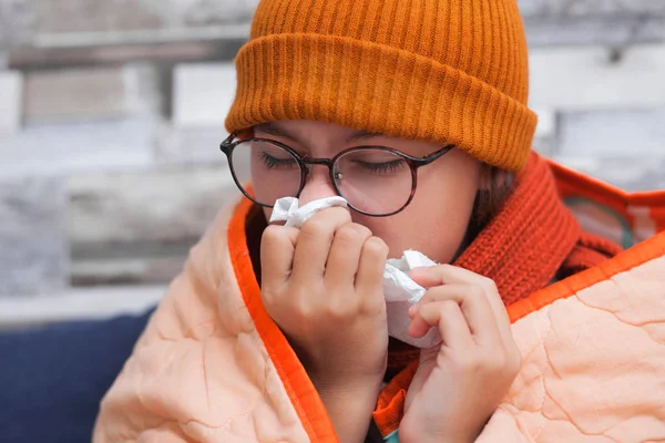 A sick teenage girl with a cold sits on a sofa and blows her nose. — 스톡 사진