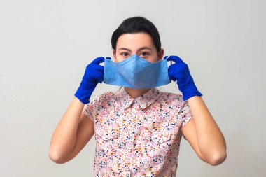 Eldivenli kız tıbbi maske takıyor. Soğuk algınlığı ve grip virüslerinin önlenmesi. Açık gri arkaplan. Solunum maskesiyle. Coronavirus ve covid-19 konsepti.