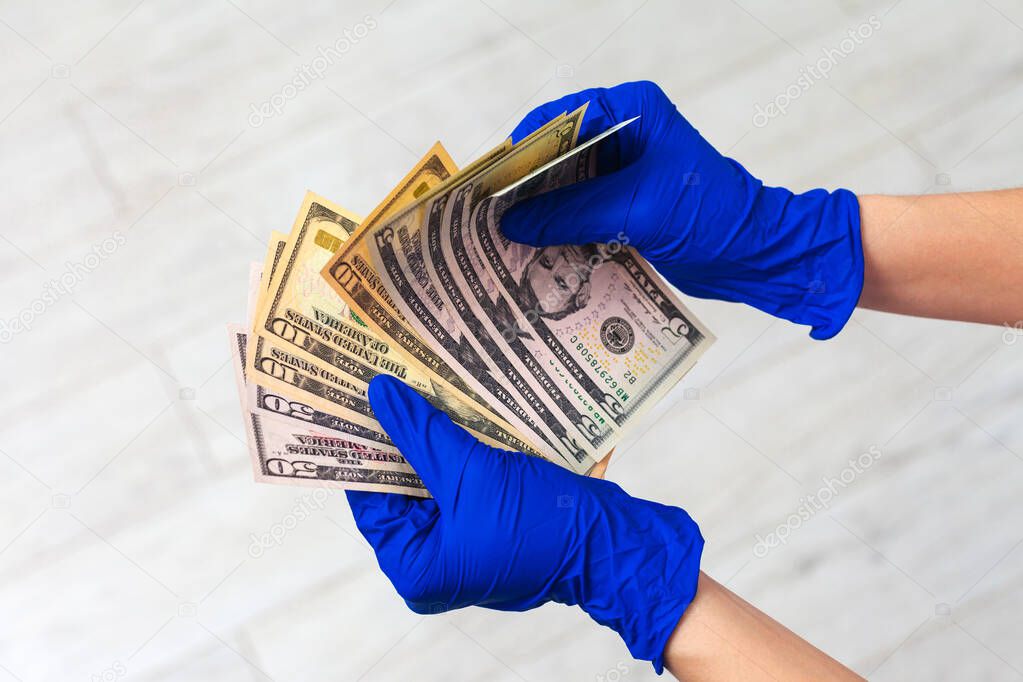 Hands in medical gloves holding a bundle of dollars. The concept of infection on money, dirty money, paid medicine, treatment fees, bribes, illegal surgery.