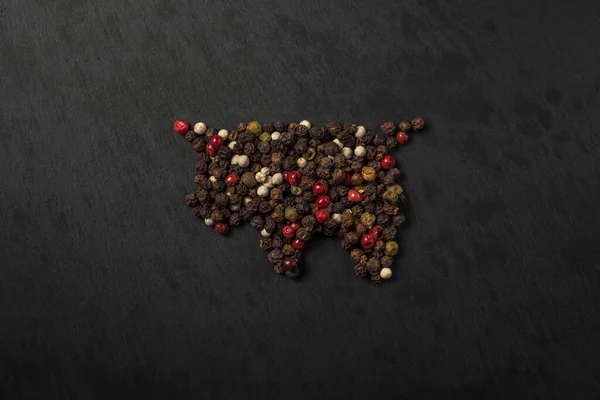 Peppercorn pepper on a black background, laid out in the shape of a bull. Red, white, green and black peppers. peas pepper. black slate background