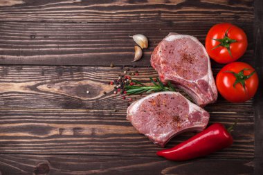 Baharatlı domuz pirzolası bifteği. Ahşap bir masanın üstünde çiğ et, domates, kırmızı biber ve biber.