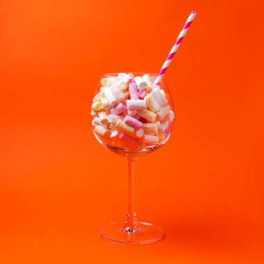 Parlak turuncu arka planda bir bardakta mini marşmelov. Bir bardakta çok renkli şekerlemeler. Şekerleme konsepti. Yan görüş. Uzayı kopyala Yakın plan.