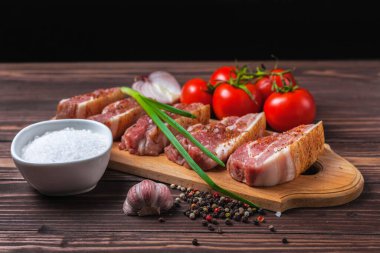 Kırsal ahşap bir masanın üstünde, kesme tahtasının üzerinde çiğ domuz pastırması dilimleri. Sebzeli domuz göbeği..