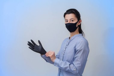 Koruyucu tıbbi maskeli ve eldivenli bir kız. Soğuk algınlığı ve grip virüslerinin önlenmesi. Açık gri arkaplan. Solunum maskesiyle. Virüs koruması kavramı.