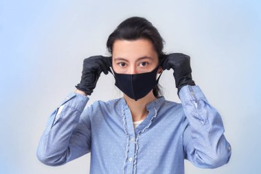 Eldivenli kız tıbbi maske takıyor. Soğuk algınlığı ve grip virüslerinin önlenmesi. Açık gri-mavi arka plan. Solunum maskesiyle.