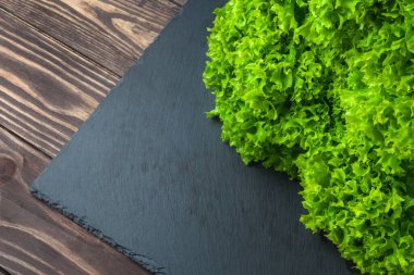 Salatalı arka plan. Tahta bir masanın üstünde, siyah bir levhada duran bir sürü yeşil marul. Taze meyve suyu.