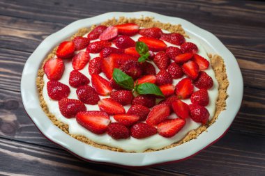 Fesleğen yapraklı çilekli cheesecake, ahşap arka planda kırmızı seramik bir fırın kabında.