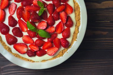 Fesleğen yapraklı çilekli cheesecake, ahşap arka planda kırmızı seramik bir fırın kabında.