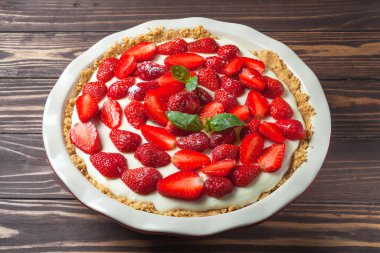 Fesleğen yapraklı çilekli cheesecake, ahşap arka planda kırmızı seramik bir fırın kabında.