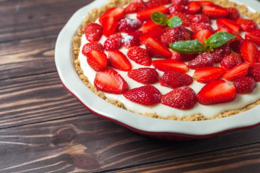 Fesleğen yapraklı çilekli cheesecake, ahşap arka planda kırmızı seramik bir fırın kabında.