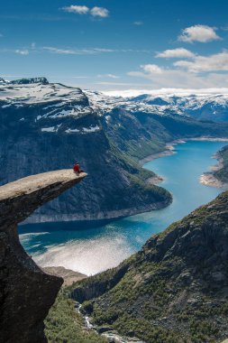 Hiker Couple sitting on a cliff over a lake, Trolltunga, Norway Concept of adventure, freedom and extreme lifestyle clipart