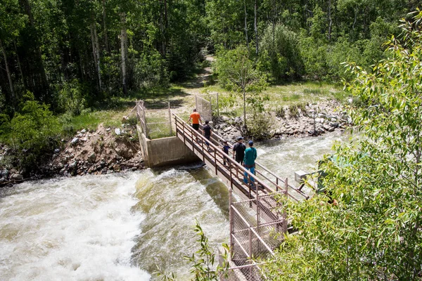 Group of tourist friends crossing the bring over rushing river, Colorado, USA