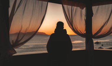 Balkondan bir adamın silueti ve deniz manzarası.