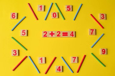 Sarı arka planda ahşap sayılar. İlkokul, birinci sınıf. Matematik. İki artı iki dört eder.