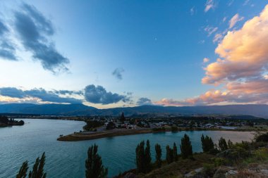 Aydınlatılmış tepeleri olan yüksek kayalıkları olan güzel bir manzara, dağ gölündeki taşlar, yansıma, mavi gökyüzü ve gündoğumunda sarı güneş ışığı. 