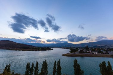 Aydınlatılmış tepeleri olan yüksek kayalıkları olan güzel bir manzara, dağ gölündeki taşlar, yansıma, mavi gökyüzü ve gündoğumunda sarı güneş ışığı. 