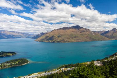 Aydınlatılmış tepeleri olan yüksek kayaları olan güzel bir manzara, dağ gölündeki taşlar, yansıma, mavi gökyüzü ve gün doğumunda sarı güneş ışığı. Tekapo, Queenstown, Wanaka.