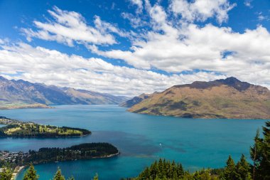 Aydınlatılmış tepeleri olan yüksek kayaları olan güzel bir manzara, dağ gölündeki taşlar, yansıma, mavi gökyüzü ve gün doğumunda sarı güneş ışığı. Tekapo, Queenstown, Wanaka.