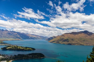 Aydınlatılmış tepeleri olan yüksek kayaları olan güzel bir manzara, dağ gölündeki taşlar, yansıma, mavi gökyüzü ve gün doğumunda sarı güneş ışığı. Tekapo, Queenstown, Wanaka.