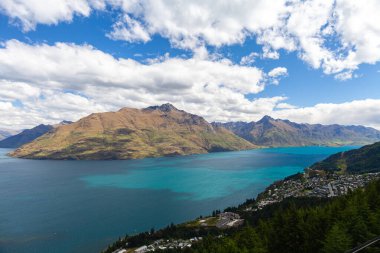 Aydınlatılmış tepeleri olan yüksek kayaları olan güzel bir manzara, dağ gölündeki taşlar, yansıma, mavi gökyüzü ve gün doğumunda sarı güneş ışığı. Tekapo, Queenstown, Wanaka.