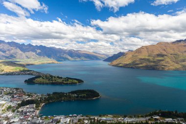 Aydınlatılmış tepeleri olan yüksek kayaları olan güzel bir manzara, dağ gölündeki taşlar, yansıma, mavi gökyüzü ve gün doğumunda sarı güneş ışığı. Tekapo, Queenstown, Wanaka.