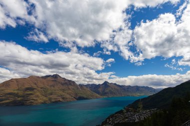Aydınlatılmış tepeleri olan yüksek kayaları olan güzel bir manzara, dağ gölündeki taşlar, yansıma, mavi gökyüzü ve gün doğumunda sarı güneş ışığı. Tekapo, Queenstown, Wanaka.