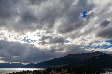 Aydınlatılmış tepeleri olan yüksek kayaları olan güzel bir manzara, dağ gölündeki taşlar, yansıma, mavi gökyüzü ve gün doğumunda sarı güneş ışığı. Tekapo, Queenstown, Wanaka.