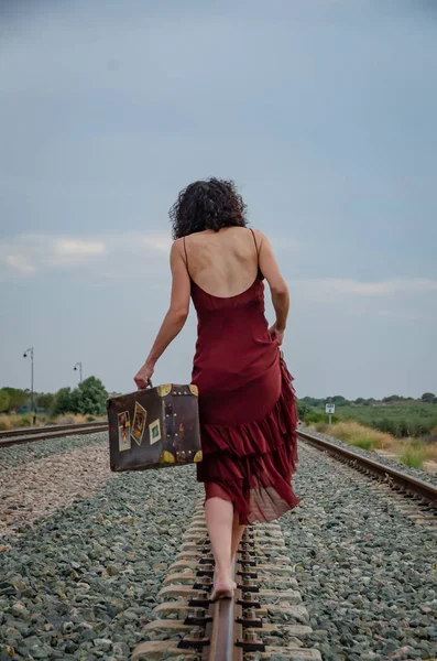 Woman with bare feet walking on the train track with a suitcase