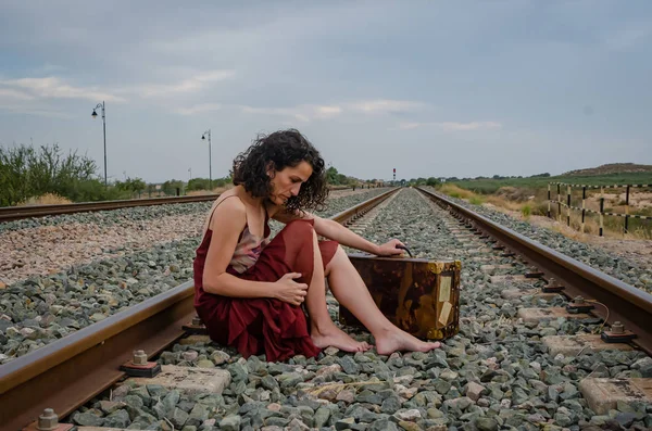 Woman with suitcase and bare feet sitting on the train track