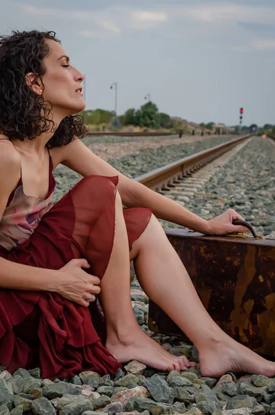 Woman with suitcase and bare feet sitting on the train track