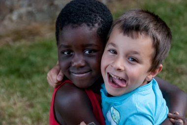 Beyaz çocuk ve siyah çocuk sarılıyor.