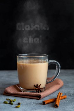 Üzerinde buhar yazan cam bir fincanda baharat bulunan Hint çayı masala çayı.
