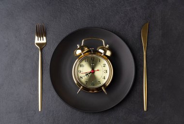 Golden alarm clock on a black plate with a golden knife and fork clipart
