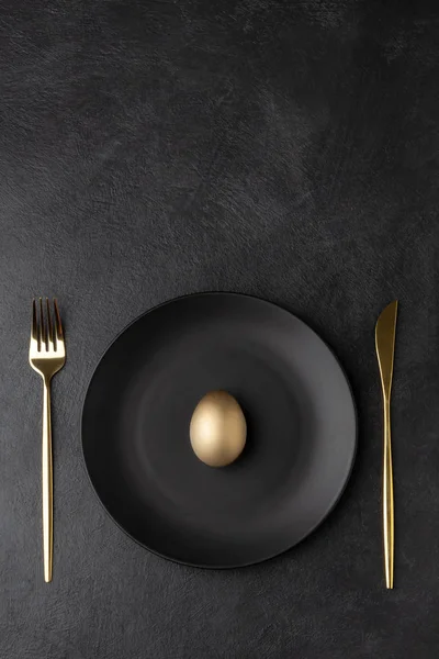 Золотое яйцо на черной тарелке с ножом и вилкой — стоковое фото