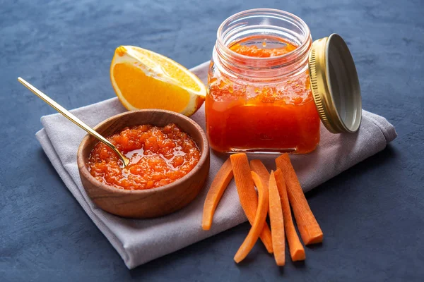 Carrot jam in a jar and a wooden bowl against a dark background — Stock Photo, Image