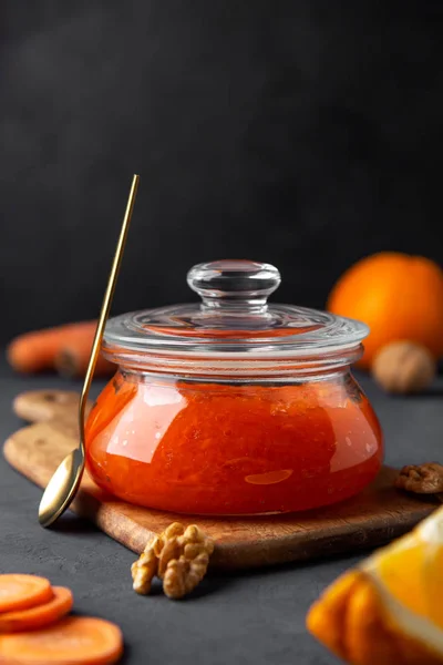 A jar of carrot jam on a cutting board with a spoon on a dark background — Stock Photo, Image