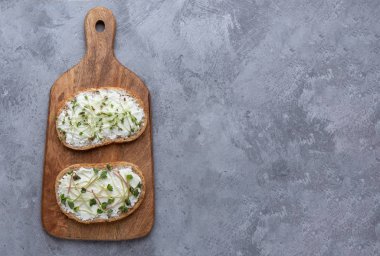 Gri arkaplandaki kesme tahtasında iki mikroyeşil sandviç.