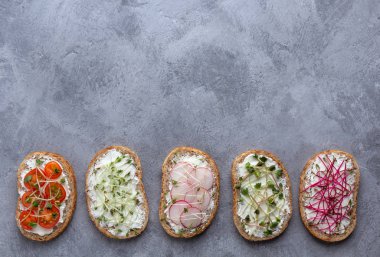 Gri arka planda peynirli, sebzeli ve mikroyeşillikli vejetaryen sandviçleri olan bir daire.