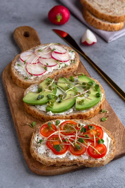 Сэндвичи с микрозеленью и овощами на доске для резки на бетонном фоне — стоковое фото