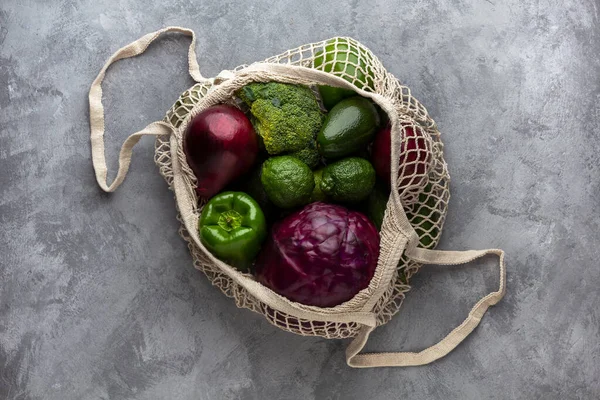 Grüne und lila Produkte in einer Öko-Tasche auf grauem Hintergrund — Stockfoto