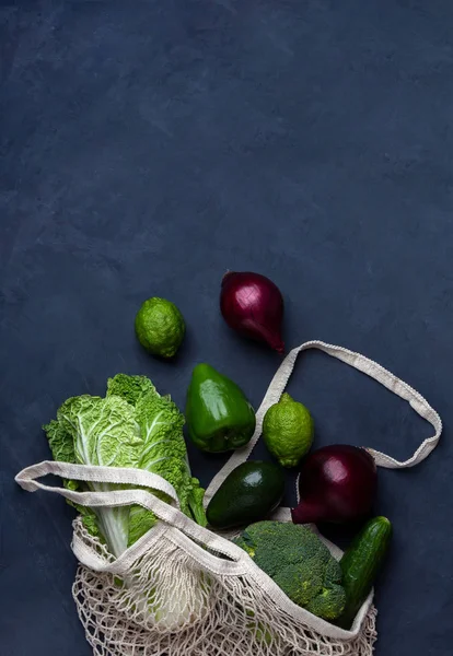 Gemüse und Obst in einer Netztasche auf dunkelblauem Hintergrund — Stockfoto